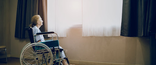 Woman in a wheelchair facing out a window and dealing with nursing home negligence. 