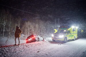 Winter car accident on slippery road at night with heavy snow fall and paramedic ambulance first aid car